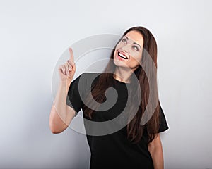 Beautiful excited casual woman in black t-shirt pointing the finger up with toothy smiling on empty copy space. Closeup