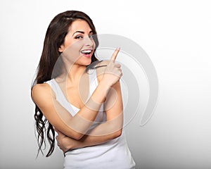 Beautiful excited casual woman pointing the finger up and smiling on white background