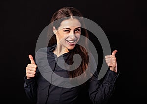 Beautiful excited energetic smiling business woman showing fingers thumb up, the ok sign in blue shirt on black background.