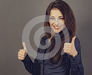 Beautiful excited energetic smiling business woman showing fingers thumb up by two hands, the ok sign in blue shirt on grey