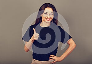 Beautiful excited energetic smiling casual woman showing finger thumb up by hand, the ok sign in blacl shirt on grey light studio