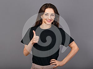 Beautiful excited energetic smiling casual woman showing finger thumb up by hand, the ok sign in blacl shirt on grey light studio