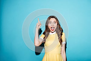 Beautiful excited girl in dress pointing finger up at copyspace