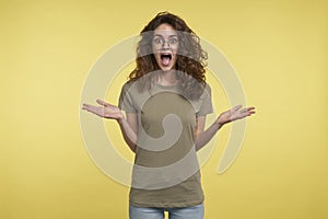 Beautiful excited and joyful young brunette female in eyeglasses and t-shirt gestures with hands and wide opened mouth