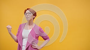 Beautiful excited middle aged redhead woman flexing her muscles, isolated on orange background