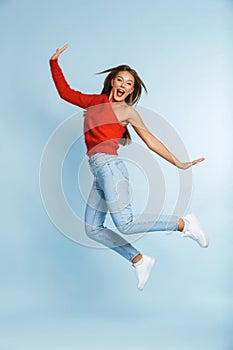 Beautiful excited young woman jumping isolated over blue wall background