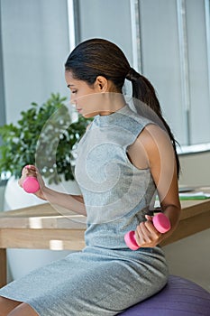Beautiful executive lifting dumbbells while exercising on fitness ball