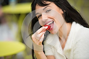 Beautiful exited woman eating strawberry lunch out of office on city street on public place.