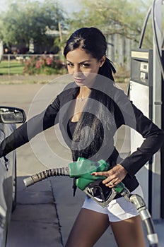 Beautiful exotic young woman pumping gas