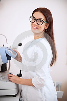 Beautiful eye doctor smiling while operating an auto refractometer