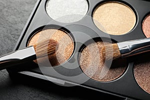 Beautiful eye shadow palette with brushes on dark grey textured table, closeup