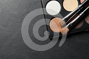 Beautiful eye shadow palette with brushes on dark grey textured table, top view. Space for text