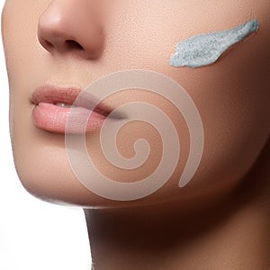 Beautiful face of young woman with cosmetic cream on a cheek. Sk