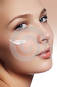 Beautiful face of young woman with cosmetic cream on a cheek. Sk
