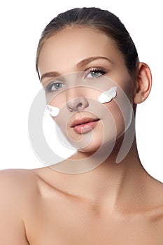 Beautiful face of young woman with cosmetic cream on a cheek. Sk