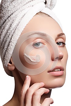 Beautiful face of young woman with cosmetic cream on a cheek. Skin care concept. Closeup portrait isolated on white. Close-up