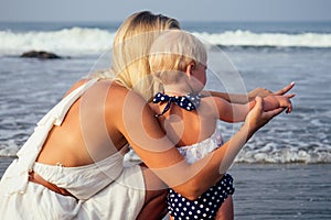 Beautiful fair-haired mother hug daughter on the sea beach. Happy family in vacation and travel. Mom show to her child