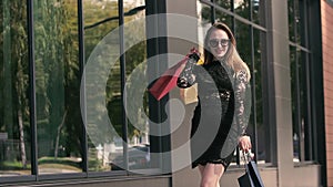 Beautiful fair-skinned young lady in black dress moves shopping bags