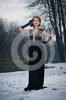 Beautiful fairy-tale winter queen in the forest with sparkling tiara and Elegant black fur coat.
