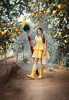 Beautiful fairytale fantasy woman holding large brown paintbrush yellow paint in hands. Girl in short dress rubber boots