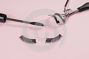 Beautiful false eyelashes, curlers and a brush on a pink background