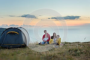 Beautiful family, camping on a hill, enjoying the sunset view on a summer day