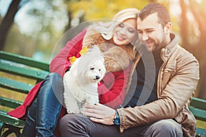 Beautiful family couple with white cute Maltese dog spending time in autumn park.