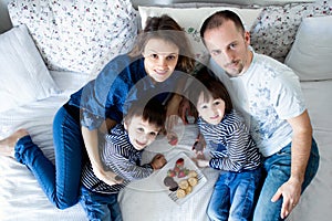 Beautiful family of four, lying on the bed, eating strawberries