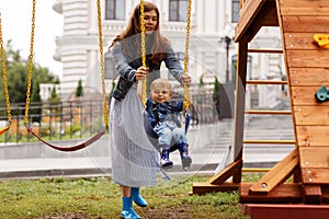 Beautiful family is having fun outside. Mama with her sun riding on a swing. Mom is playing with her little son on a terrace with