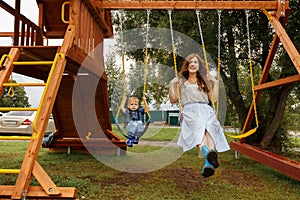 Beautiful family is having fun outside. Parents with children riding on a swing. Mom is playing with her little son on a terrace