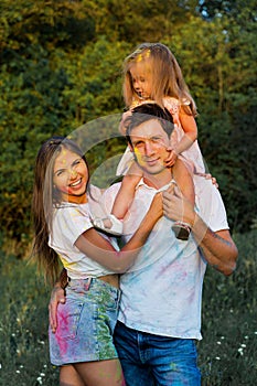 Beautiful family, mom, dad and daughter play with Holly colors. multi-colored paint on clothes and face
