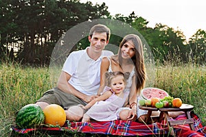 Beautiful family, mom, dad and daughter sitting on a picnic with watermelon