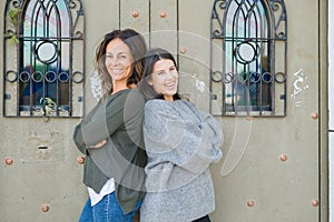 Beautiful family of mother and daughter with crossed arms smiling cheerful, two happy women together leaning on each other as