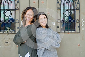 Beautiful family of mother and daughter with crossed arms smiling cheerful, two happy women together leaning on each other as