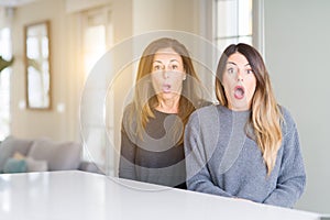 Beautiful family of mother and daughter together at home afraid and shocked with surprise expression, fear and excited face
