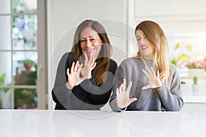 Beautiful family of mother and daughter together at home disgusted expression, displeased and fearful doing disgust face because