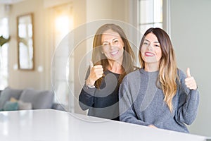 Beautiful family of mother and daughter together at home doing happy thumbs up gesture with hand