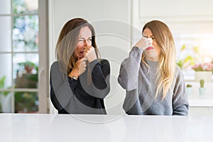 Beautiful family of mother and daughter together at home smelling something stinky and disgusting, intolerable smell, holding