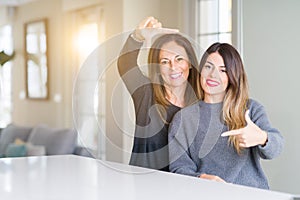 Beautiful family of mother and daughter together at home smiling making frame with hands and fingers with happy face