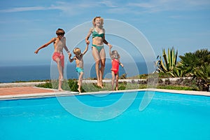 Beautiful family in motion by pool, laugh and jump together