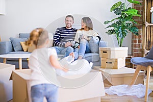 Beautiful family, parents sitting on the sofa drinking coffee looking his kid playing at new home around cardboard boxes