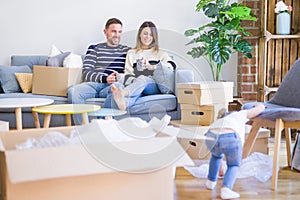 Beautiful family, parents sitting on the sofa drinking coffee looking his kid playing at new home around cardboard boxes
