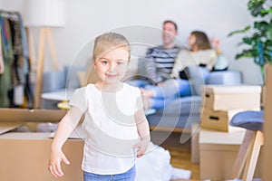 Beautiful family, parents sitting on the sofa drinking coffee looking his kid playing at new home around cardboard boxes