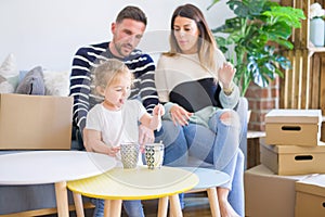 Beautiful family, parents sitting on the sofa drinking coffee looking his kid playing at new home around cardboard boxes