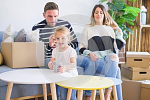 Beautiful family, parents sitting on the sofa drinking coffee looking his kid playing at new home around cardboard boxes