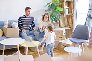 Beautiful family, parents sitting on the sofa drinking coffee looking his kid playing at new home around cardboard boxes