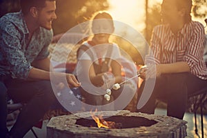 Beautiful family of three roasting marshmallows together by a fireplace, sitting in cozy chairs outdoors