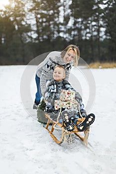 Beautiful family of young mother and son enjoying snowy winter day outdoors having fun sledging. Boy is sitting on the