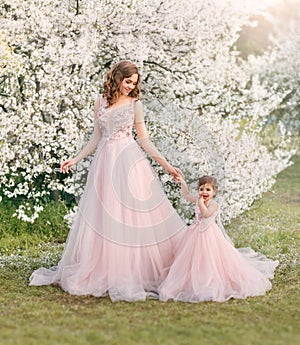 Beautiful fantasy woman gently holds hand little cheerful smiling girl. Happy family mom and daughter walk in blooming