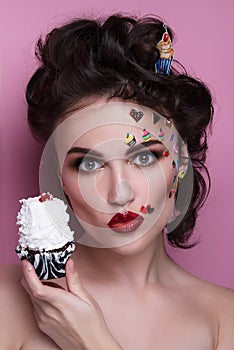 Beautiful fashion girl with luxury professional makeup and funny emoji stickers glued on the face. Young woman with cupcake.